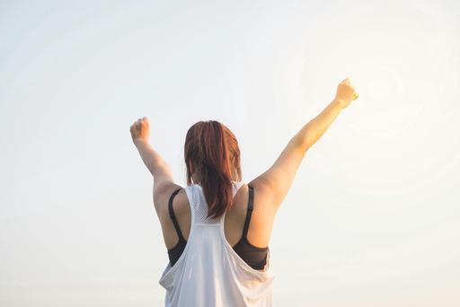 back of woman stretching arms up at sunrise